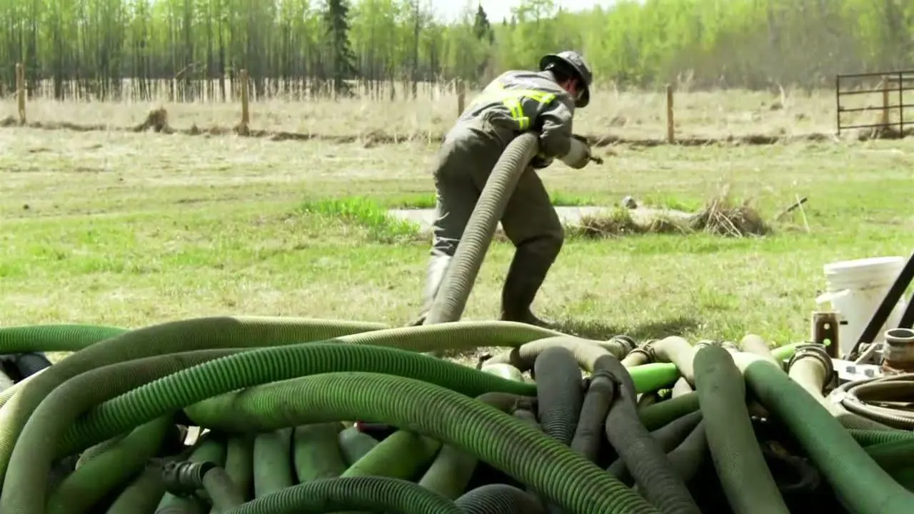 Trabajador arrastrando a mano una manguera de succión junto a un montón de mangueras en terreno