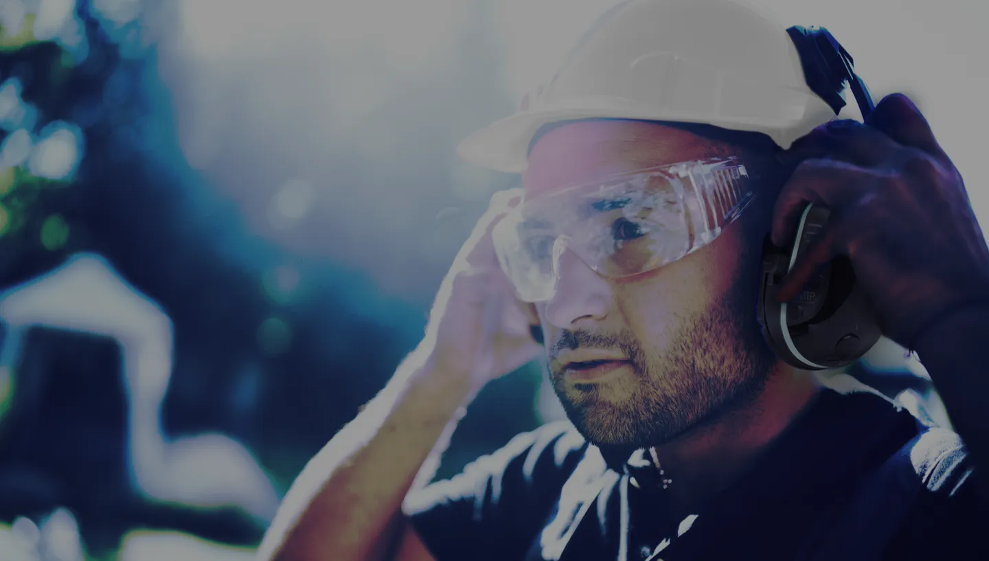 Trabajador con casco y lentes de seguridad usando un audífono de comunicación Sensear