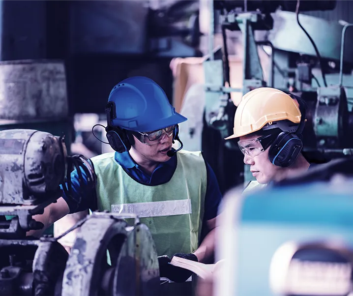 Dos trabajadores con audífonos Sensear conversando junto a una máquina en planta